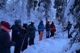 人们穿着冬装，拿着一根长长的白色管子，在白雪皑皑的森林中测量土壤霜冻. 