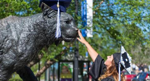 Newly graduated student patting the wildcat statue's nose.
